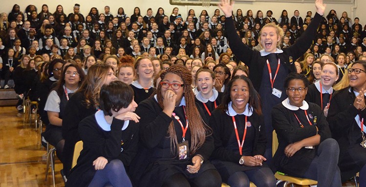 Catholic school students in joyful assembly as one student stands with her hands raised in jubilation.